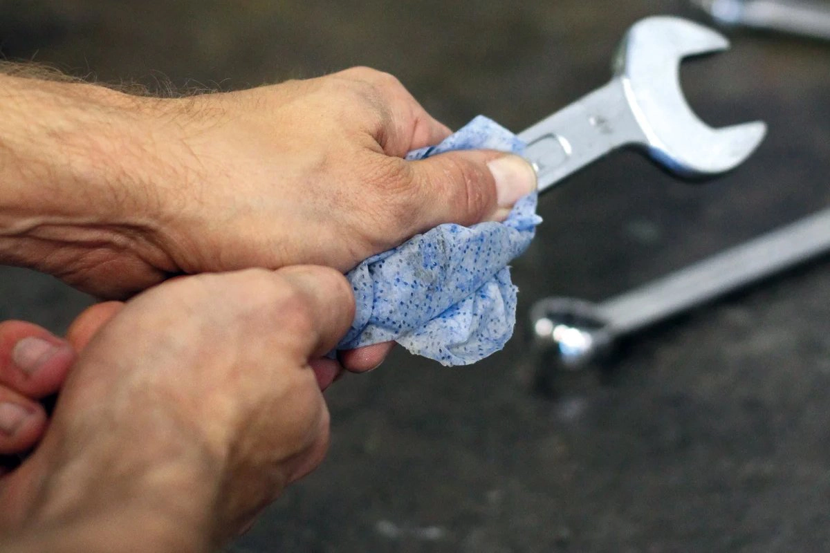 Person vasker skiftenøkkel med SCRUBS håndrens-servietter i verksted.